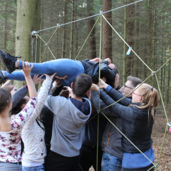 Wirtschaftsakademie – Teamtraining schweißt zu Beginn des Akademiejahres die Teilnehmer zusammen. Hier wrd gemeinsam eine Person durch eine gespannte Öffnung in ein Meter Höhe getragen.