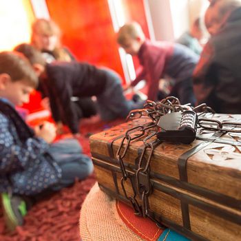 Spielmobil Bayreuth – Kinder spielen im Hintergrund, im Vordergrund die mit Ketten und einem Zahlenschloss verschlossene Schatztruhe, das Ziel des Exit Games.