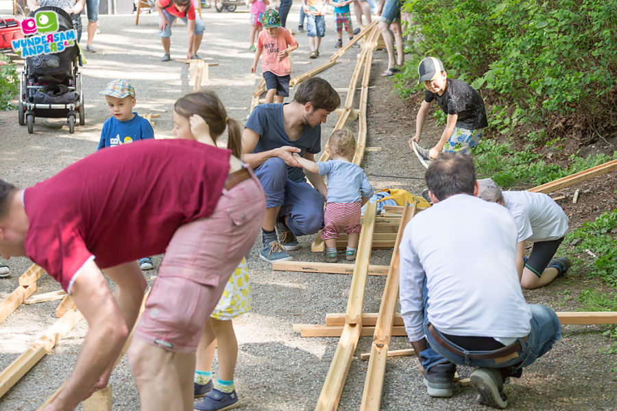 Eltern bauen im Freien mit ihren Kindern eine riesige Holz-Murmelbahn auf.