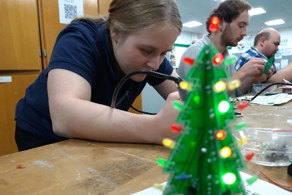 Mehrere Personen beim Elektroniklöten. Im Vordergrund leuchtet ein schon fertiger kleiner Weihnachtsbaum