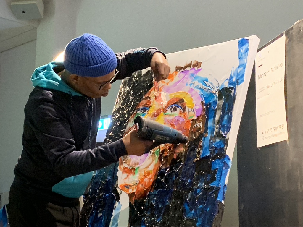 Ein Kunstschaffender bearbeitet mit einem Föhn ein buntes Gemälde