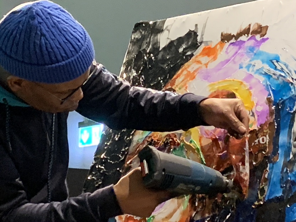 Ein Kunstschaffender bearbeitet mit einem Föhn ein buntes Gemälde